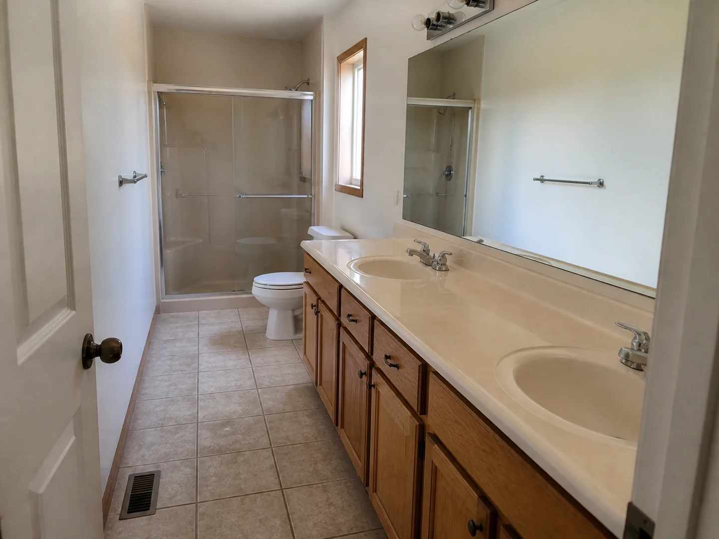 Dated narrow primary bathroom with long oak vanity and shower